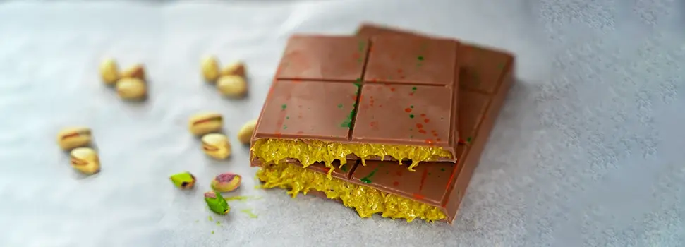 A creamy milk chocolate bar with a vibrant pistachio filling, adorned with colorful splashes.